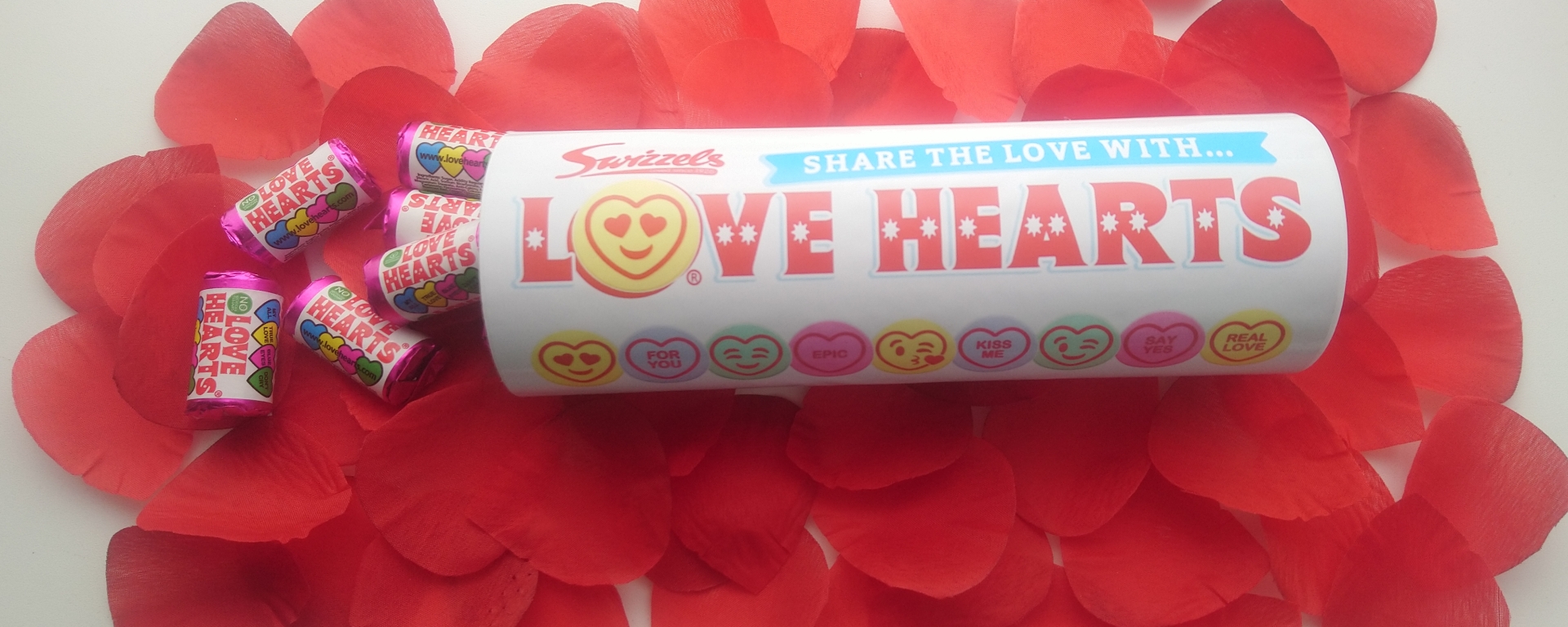 A tube of sweets on a bed of rose petals, with some packets of sweets pouring out.